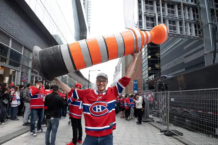 Fan holding giant Stanley Cup-shaped traffic cone at hockey game.